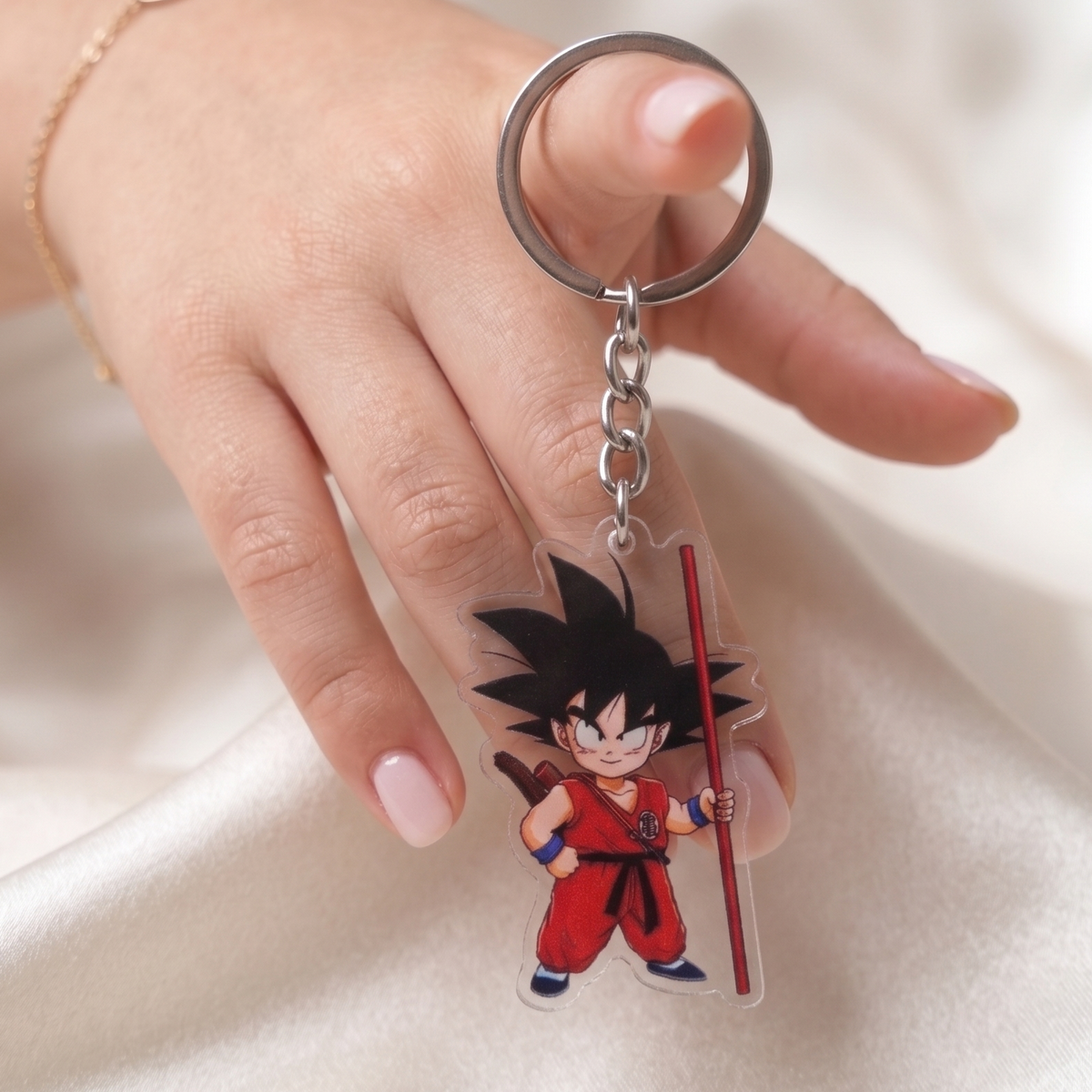 Hand holding a Kid Goku Dragon Ball clear acrylic anime keychain against a smooth silk background