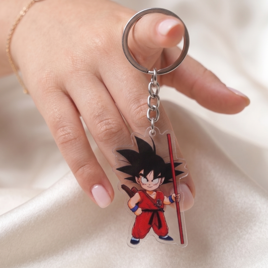 Hand holding a Kid Goku Dragon Ball clear acrylic anime keychain against a smooth silk background