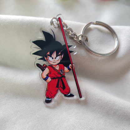 Kid Goku Dragon Ball clear acrylic keychain resting on textured white fabric with pink flowers in the background