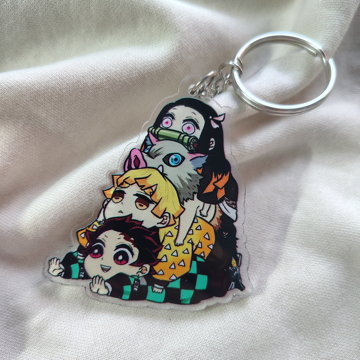 Clear acrylic Demon Slayer Kimetsu no Yaiba group character keychain lying flat on soft white fabric