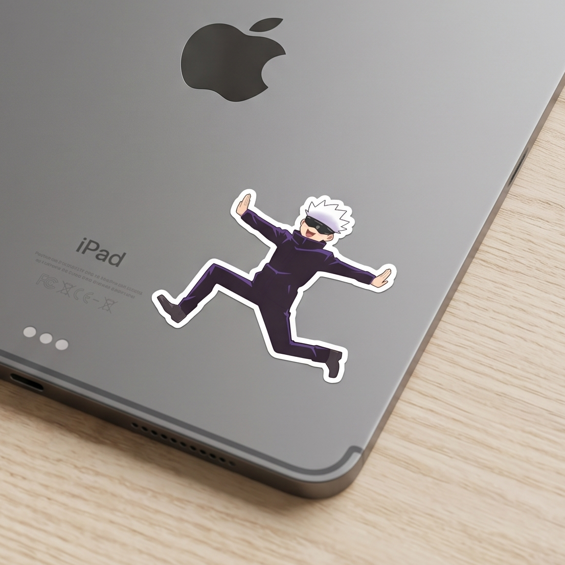 A die-cut vinyl sticker of the anime character Gojo Satoru Gojo from Jujutsu Kaisen, shown applied to the back of a gray iPad on a light wood surface.
